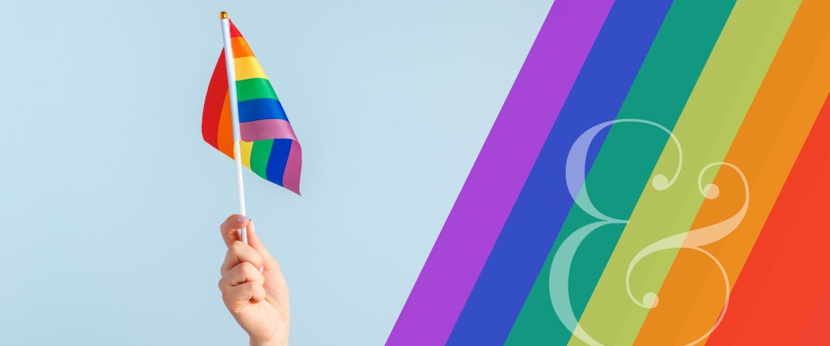 Graphic features a hand holding up a rainbow Pride flag and a rainbow design to the right of the image.