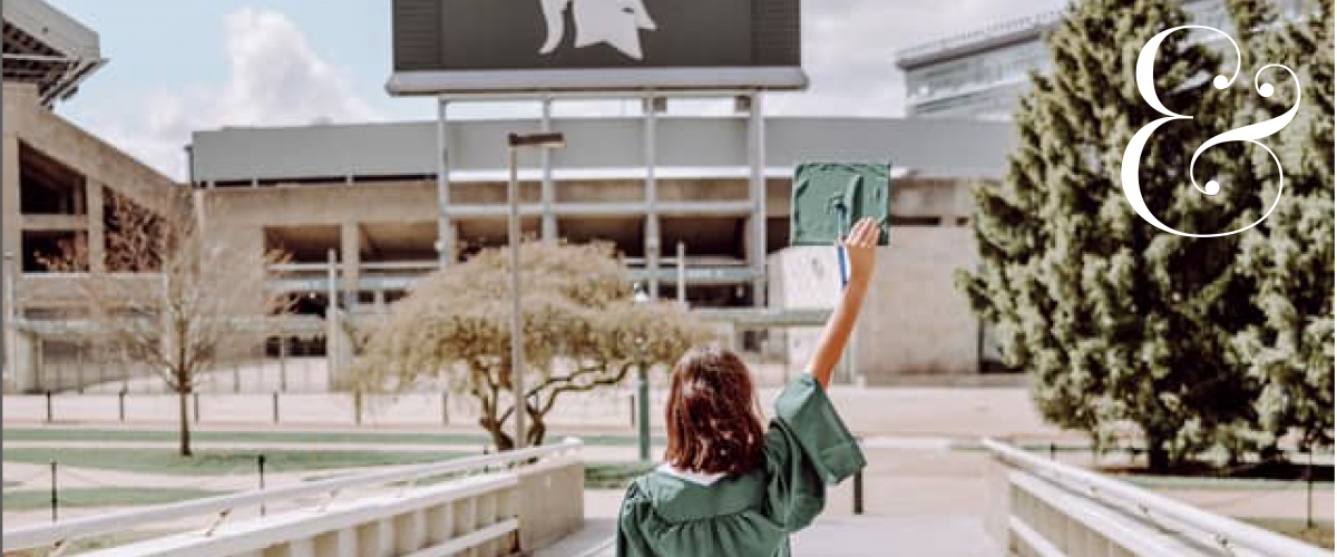 Image features a student in a green cap and gown in front of the MSU football stadium.