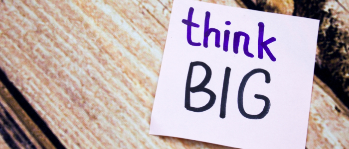 A purple note sits in front of a wooden background. The note's text says "think big."